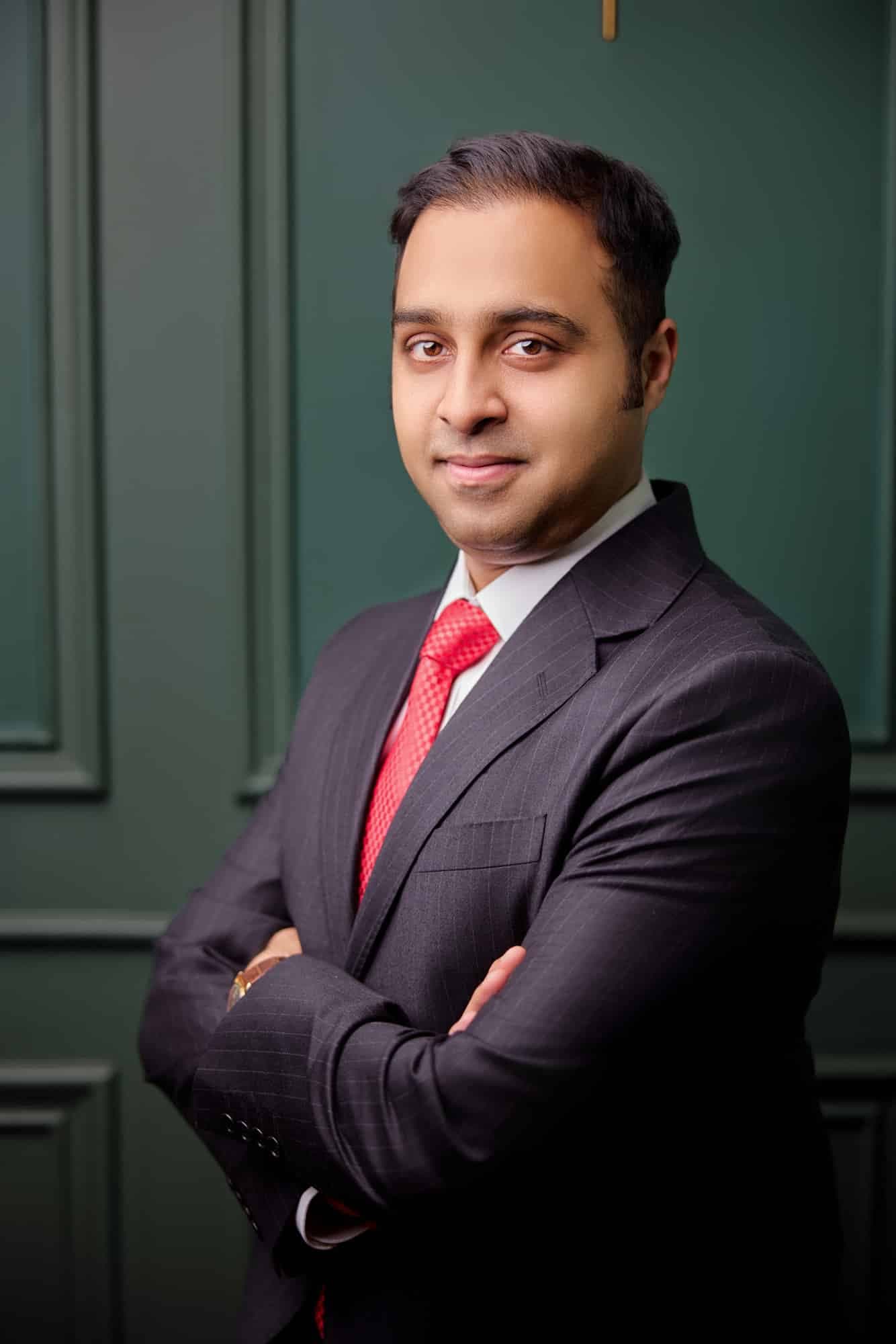 Executive in a navy suit with arms crossed against a dark green wall