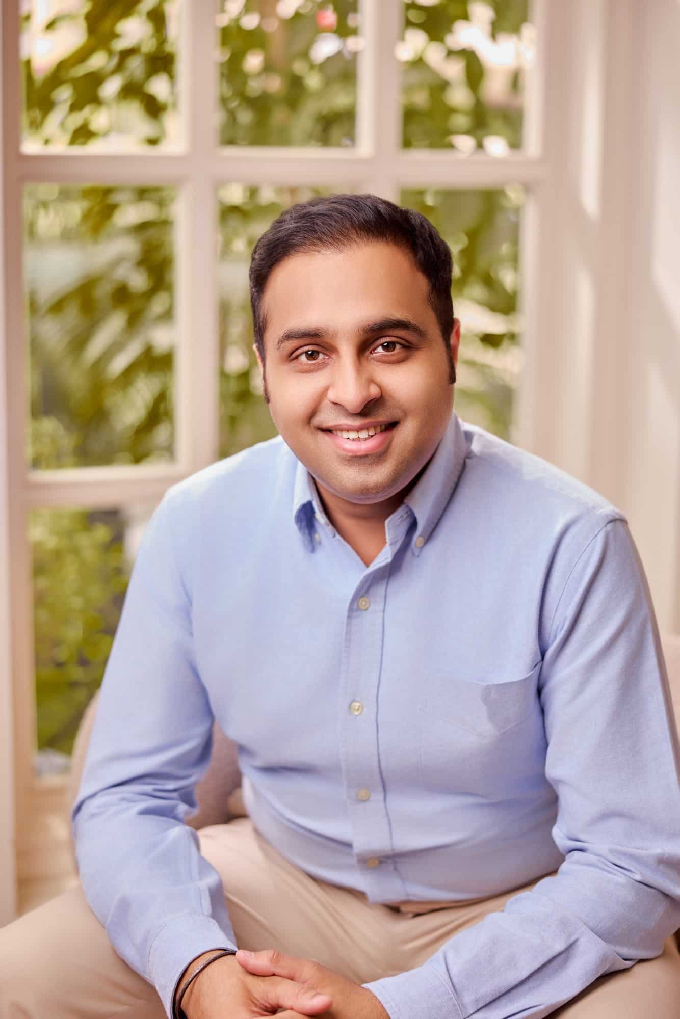Executive portrait of a smiling professional in a blue shirt beside a sunlit window