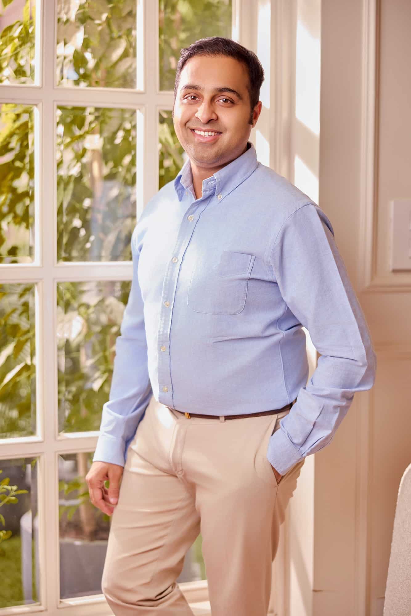 Founder in a blue shirt standing by sunlit French windows
