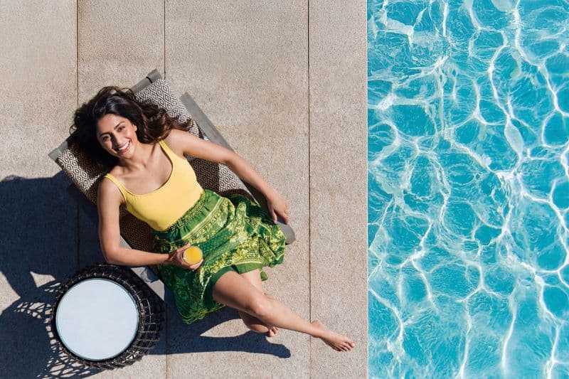 Aerial lifestyle portrait of a woman on a sun lounger beside a pool