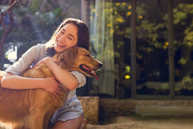 Woman embracing her golden retriever in a garden — candid lifestyle portrait