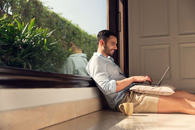 Man working on a laptop by a sunlit window at a luxury residence